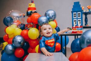 פעוט מחויך בחליפה צבעונית בין בלונים צבעוניים ומגדל כחול קטן ברקע מתאים לאתר דפי צביעה לילדים ופעילויות יצירה שילדים יאהבו